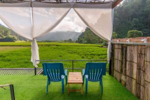 Pang Maphaเนเจอร์วัลเล่ย์แคมป์ ปางมะผ้า的门廊上设有两把椅子和一张桌子,享有田野美景