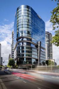 墨尔本Adina Apartment Hotel Melbourne Southbank的前面有汽车的一座高大的玻璃建筑