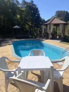 卡洛斯-巴尔博萨Sítio dos Coqueiros, em meio a natureza com piscina的游泳池旁的白色桌椅
