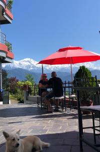 博卡拉Hotel Pristine Himalaya的两个人坐在桌子下,被一只狗放在伞下