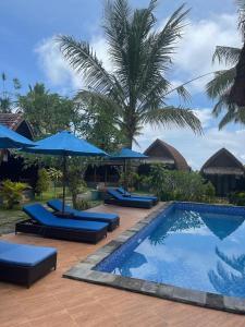 珀尼达岛Kelingking Tatakan Bungalow的一个带蓝伞的游泳池和一个度假村