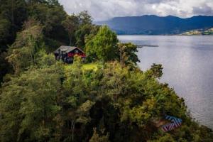 帕斯托Cabaña Colibri naturaleza vista Laguna de la Cocha的水体旁山丘上的房屋