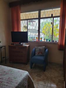 里约热内卢Casa aconchegante em Vila Valqueire的一间卧室配有电视、椅子和窗户