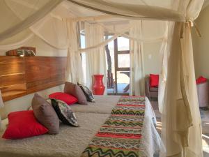 奥乔Okutala Etosha Lodge的一间卧室配有一张带红色枕头的天蓬床
