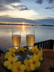 东德岛Don Det Hotel的两杯酒和鲜花,放在桌子上,水边
