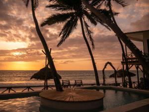 布韦朱KIMA Serviced Beach House & Suites的海滩上的日落,游泳池,棕榈树