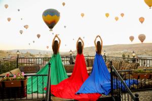 格雷梅Göreme Reva Hotel的三个穿着五颜六色衣服的女人看着热气球