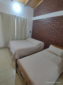 PuelchesHotel Juanita的一间卧室设有两张床和砖墙