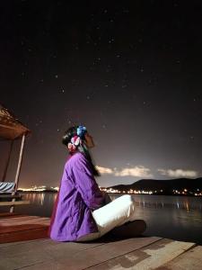 普诺Uros Walysuma Titicaca Lodge的一位坐在码头上,晚上看着水面的女人
