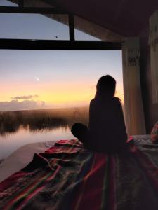 普诺Uros Walysuma Titicaca Lodge的坐在床上看着日落的女人
