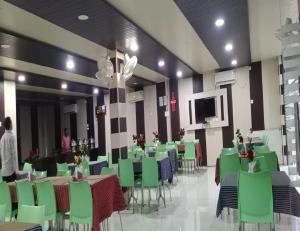 王舍城Hotel Glory Grand, Rajgir的一间带绿色桌椅和电视的用餐室
