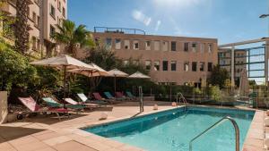 土伦土伦市中心假日旅馆的一座带椅子和遮阳伞的游泳池位于一座建筑旁边
