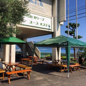 小豆岛小豆岛橄榄青年旅舍的一组野餐桌,在建筑外摆放着绿伞