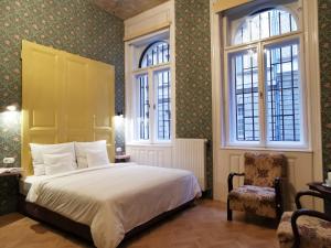 布达佩斯Metropolis Budapest的一间卧室设有床、两扇窗户和一把椅子