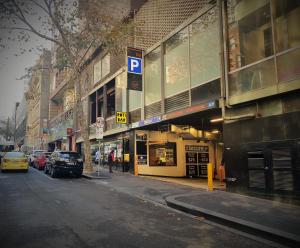 墨尔本CitiClub Hotel Melbourne的一条城市街道,汽车停在建筑前