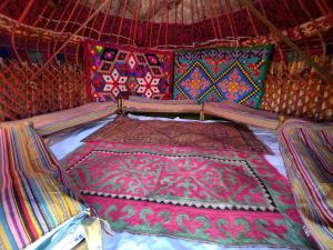 科奇科尔Son-Kul Northen yurt camp的帐篷内的一张床位,配有色彩缤纷的毯子和枕头