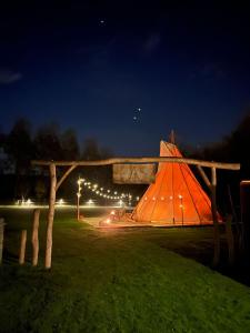 LembekeComfort Tipi Marie, Tipi Bo Deluxe & tent Nicolaï - 'Glamping in stijl'的夜晚在田野里的一个橙色帐篷