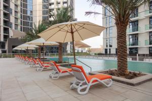 迪拜Expo Village Serviced Apartments的游泳池旁的一排椅子和遮阳伞