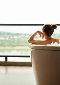 清孔Chiangkhong Teak Garden Riverfront Onsen Hotel- SHA Extra Plus的坐在窗前浴缸中的女人