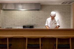 丰冈市森穗酒店的厨师站在厨房的柜台后面