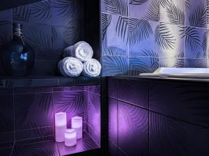 圣艾蒂安Suite Privative Rouge baiser - Spa & Jacuzzi - Love Room à Saint Etienne的紫色浴室,配有毛巾和架子上的蜡烛