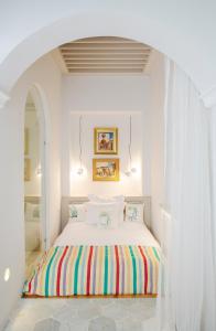 突尼斯Dar Dorra的白色卧室配有一张带彩色毯子的床