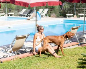 卡波利韦里Country Hotel Residence Da Pilade的坐在椅子上的女人和狗一起坐在游泳池边
