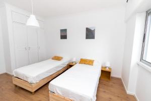 PaiõisAL Cacém的配有白色墙壁和木地板的客房内的两张床