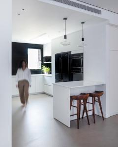 特拉维夫12 Shimon HaTzadik - By Beach Apartments TLV的一位妇女穿过一个厨房,厨房里装有白色的橱柜