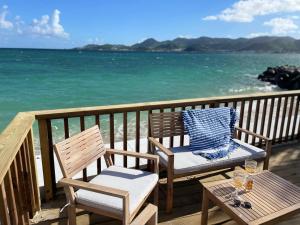 Baie NettleLa Plage Bleue feet in the water with swimming pool的阳台上配有两把椅子和一张桌子,享有海景