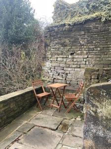 霍姆弗斯Brook Cottage的一张桌子和两把椅子,坐在石墙旁边