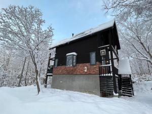 二世古Goodfellas Onsen House的雪中的一个黑色小屋,有雪覆盖的树木