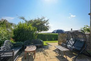 阿尼克Mossyford Cottage的庭院设有2张长椅、桌子和遮阳伞