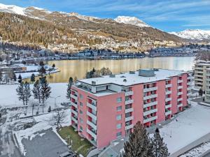 圣莫里茨Abitaziun Skyline 414 - St Moritz "LOGA ELEGANCE APARTMENT"的水体前的粉红色公寓楼