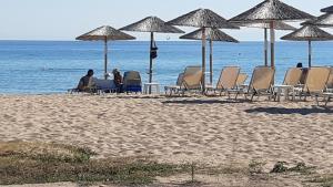 尼亚普拉加ammos seafront family apartments的坐在海滩上遮阳伞下椅子上的人