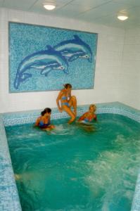 吉奥马恩德勒德Hárs Thermál Hotel的三个女人在游泳池里,墙上有海豚