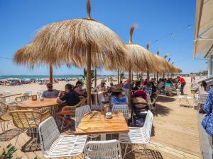 圣玛丽亚港Valdelagrana vistas al mar, piscinas primera linea cadiz的一群人坐在海滩上,坐在遮阳伞下的桌子上