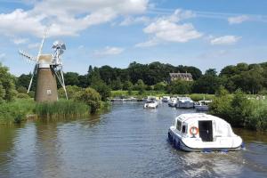 大雅茅斯'Sunnyside' Chalet, walk to the beach & close to Norfolk broads - pet friendly!的风车旁边的水中的小船