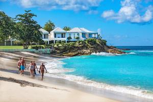 Five Islands VillageHawksbill Resort Antigua - All Inclusive的一群人在房子前面的海滩上散步