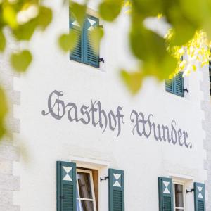 Auna di SottoGasthof Wunder的白色建筑的侧面标牌,带有绿色窗户