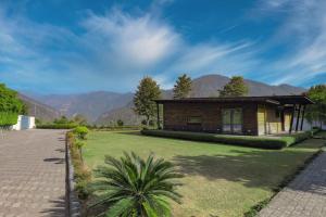 德拉敦SaffronStays Paradise Pines, Dehradun - cliff villa with valley & forest views的一座房子,旁边是草地庭院