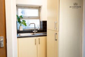 沃灵顿2 bed Apartment by UK Corporate Relocations Ltd的厨房配有白色橱柜、水槽和窗户。