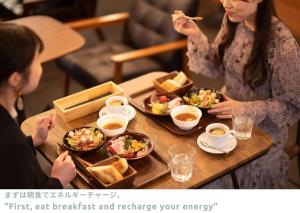 金泽LINNAS Kanazawa的两个坐在餐桌上吃食物的女人
