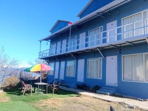 卡纳塔尔IN APPLE ESTATE KANATAL - Himalayan View Resort with Courteous Staff的蓝色的建筑,配有桌子和雨伞