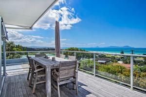 怀普Surfers Lookout - Waipu Cove Holiday Home的阳台上的木制甲板上配有桌椅