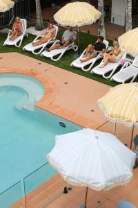 穆卢拉巴Abode Mooloolaba, Backpackers & Motel rooms的一群人坐在草地椅上,在游泳池边的伞下