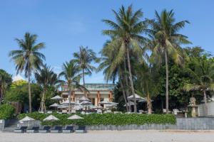 华欣Cape Nidhra Hotel的海滩上种有棕榈树和遮阳伞的度假村