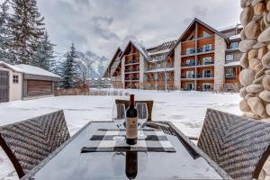 坎莫尔Mountain Retreat, Pool & Hot Tub, BBQ, Patio, King Bed, Sleeps 6!的雪覆盖的庭院里摆放着一张桌子和一瓶葡萄酒