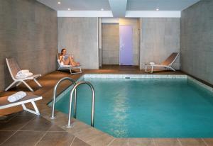蒂涅Hôtel L'Aiguille Percée的酒店客房带游泳池,两人坐在椅子上