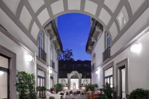 那不勒斯Hotel Piazza Bellini & Apartments的一座建筑的拱门,人们坐在庭院里